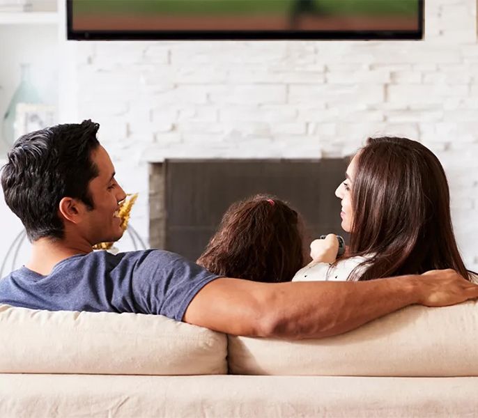 Family watching TV programming from their living room couch, viewed from behind