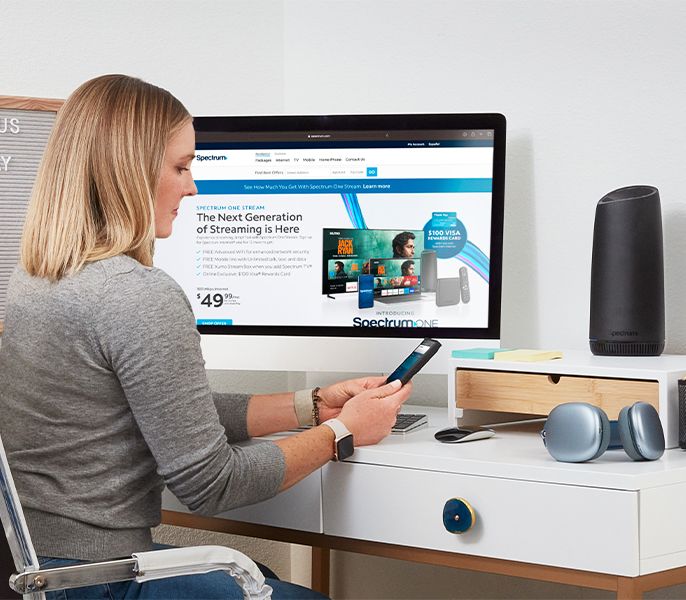 Woman using her mobile phone at her desk at home, wifi router and desktop computer visible