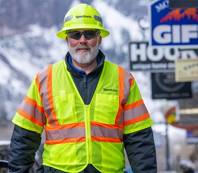 Spectrum technician walking through downtown Telluride, past shops and businesses, with yellow safety vest on