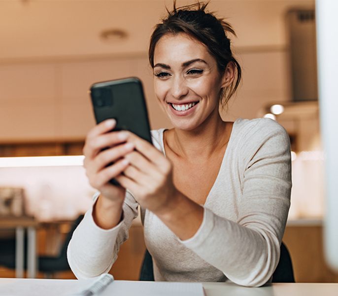 Woman using her mobile phone at her desk at home, smiling